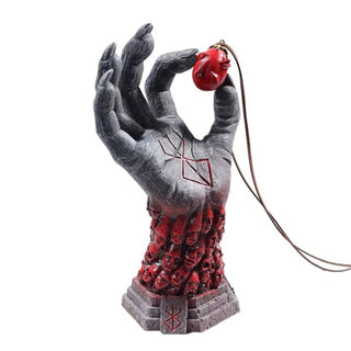 A Berserk collectible figurine of a skeletal hand holding a red heart, with red skulls cascading down a stone base