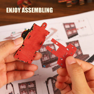 Red laser-cut wooden model pieces held by hands with assembly instructions in the background.