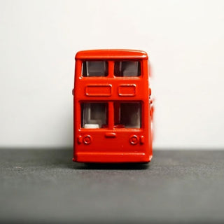 Red toy double-decker bus on a gray surface with a white background